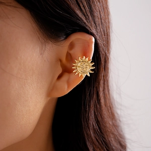 Close-up of a vintage golden sun face ear cuff clipped onto the ear without piercing