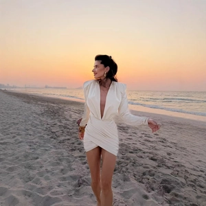 Elegant white long sleeve mini dress with deep V-neck and ruched details on beach