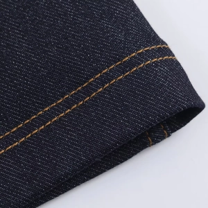 Vista macro del tessuto denim blu scuro con doppie cuciture gialle rinforzate sull'abito