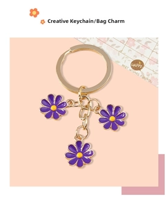 Close-up of golden keychain with three purple enamel daisy charms on pink background