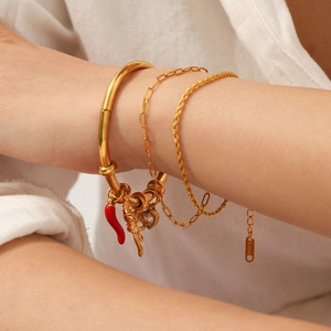 Detail of layered gold stainless steel bracelets with chili and unicorn charms on wrist