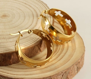 Close-up of golden stainless steel wide hoop earrings with hollow cross patterns on wood