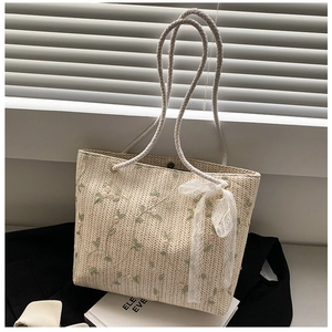 Close-up of straw woven tote with floral embroidery, lace bow, and soft cotton handles