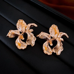 Detailed view of golden flower earrings with pleated metal texture on a textured base