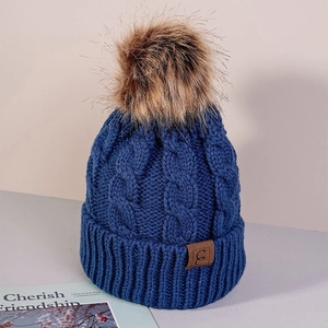 Close-up of blue cable knit beanie with faux fur pom-pom and leather patch detail