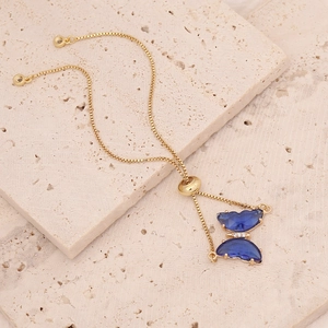 Macro detail of 18K gold box chain bracelet with blue gemstone butterfly pendant