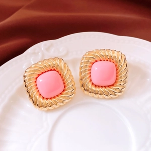 Macro shot of vintage gold square twisted earrings with pink inlay on a white plate