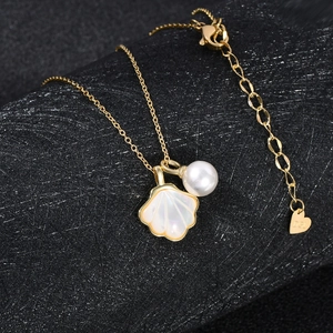 Macro shot of gold shell pendant with white pearl and DGL logo heart tag on gold chain