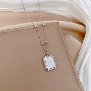 Detail of silver beaded necklace with square shell pendant on soft white silk fabric
