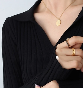 Dettaglio della collana con ciondolo a rosa dorata e anello con pietra nera su modella