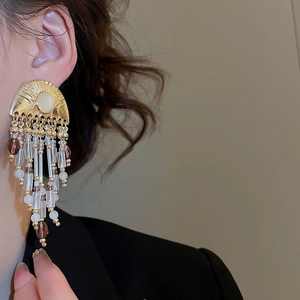 Detail view of retro gold fringe earrings with cream stones and beaded tassels on a model