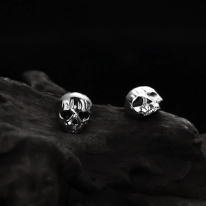 Macro shot of polished silver skull stud earrings on dark stone background