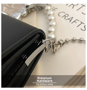 Detail of silver hardware and pearl chain strap on a black quilted leather crossbody bag