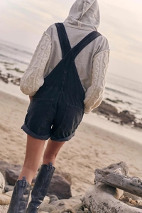 Detail of dark gray denim overalls with pockets from behind in a beach setting