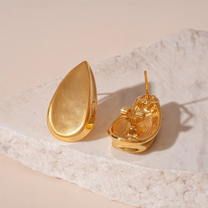Gros plan de boucles d'oreilles goutte dorées sur marbre au fini métallique brillant
