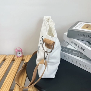 Detail view of white canvas crossbody bag with silver metal ring and brown shoulder strap