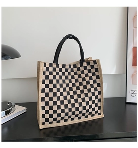 Detailed view of checkered linen tote bag with black woven handles on a wooden table
