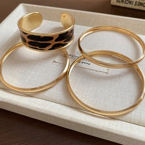 Detail of a leopard print cuff and gold bangles set displayed on a textile jewelry tray