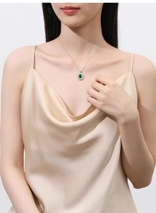 Close-up of a silver necklace with a green round gemstone pendant on a model's neck