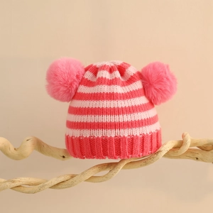 Dettaglio del cappello in maglia a righe rosa per neonati con due pompon e supporto in legno