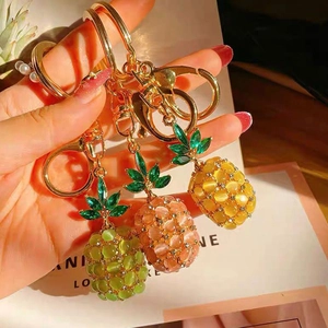 Close-up of cat-eye pineapple keychains in green, pink and amber with gold plating