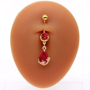 Dettaglio del piercing all'ombelico dorato con pietra rossa a goccia e fiori