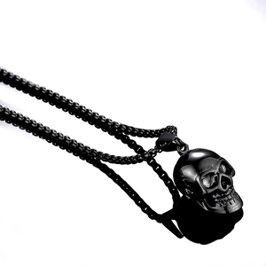 Detailed view of a black metal skull pendant on a matching box chain over white background