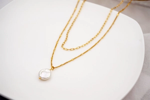 Detail view of double-layer gold chain necklace with a baroque pearl on a white ceramic plate