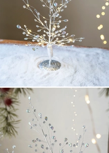 Detail of silver branch LED Christmas tree with colorful crystal drops on snowy surface