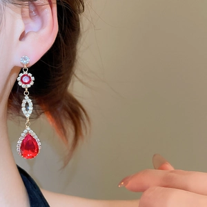 Macro detail of elegant drop earrings featuring red pear-cut crystals and pavé diamonds