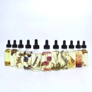 Set of 11 glass dropper bottles with assorted dried flowers and essential oils on white background