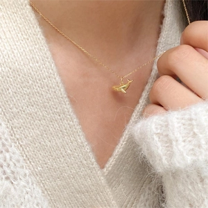 Close-up of a minimalist golden whale pendant necklace worn on a white knit sweater