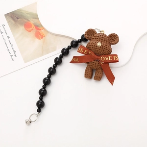 Detailed view of a brown knit teddy bear phone charm with decorative red ribbon and black beads