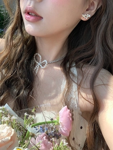 Close-up of model wearing a pearl bow necklace and flower earrings set in natural light