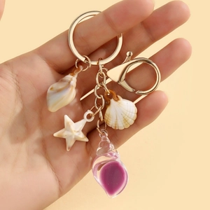 Detailed close-up of a gold keychain with resin seashell and starfish charms in hand