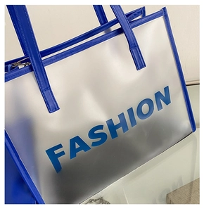 Detail of transparent frosted tote bag with blue faux leather handles and FASHION text