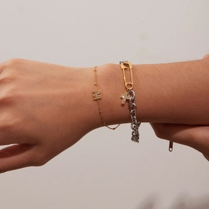Detail of gold letter M pendant and layered silver chain bracelet on model wrist