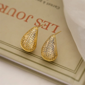 Macro detail of gold teardrop earrings encrusted with zircon on vintage book background