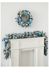 Detail of Christmas wreath and garland with blue ornaments and snow-tipped pine branches
