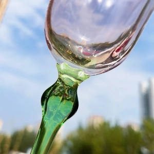 Low angle shot of a pink floral glass wine goblet with a green stem against a blue sky