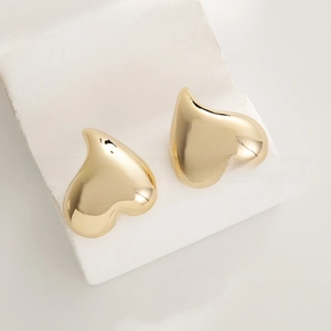Macro detail of polished gold heart stud earrings on a minimalist white stone base