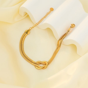 Gold double-layered snake chain bracelet with elegant knot center on silk background