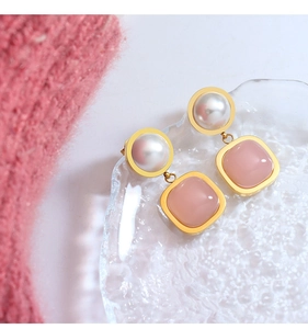 Detail of elegant gold earrings with pink square gemstones and white pearls on glass