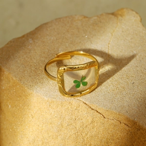 Gold stainless steel ring featuring a green four-leaf clover inlay on sandstone background