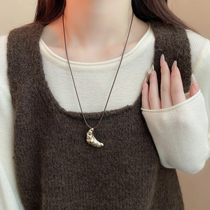 Close-up of golden croissant pendant necklace with brown leather cord on a female model