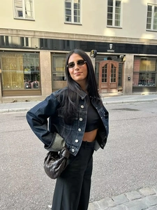 Détail d'une veste en jean bleu foncé portée avec un sac cabas en cuir tressé en ville