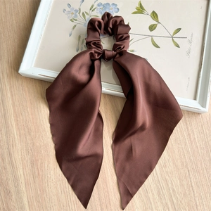 Close-up of a dark brown satin scrunchie with long ribbons on a wooden surface