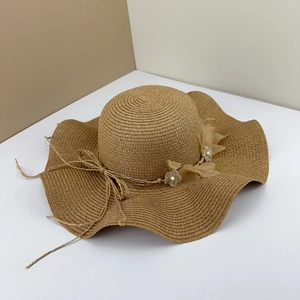 Détail du chapeau de paille à large bord ondulé avec fleur de gaze et perles