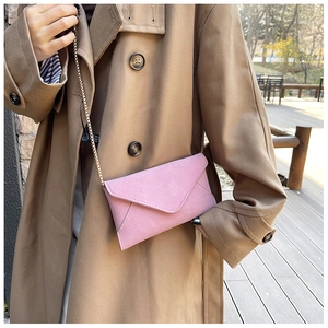 Detail of pink faux suede crossbody bag with gold chain strap worn with a khaki coat