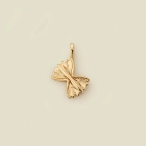 Close-up of golden farfalle pasta pendant with detailed metal texture on beige background